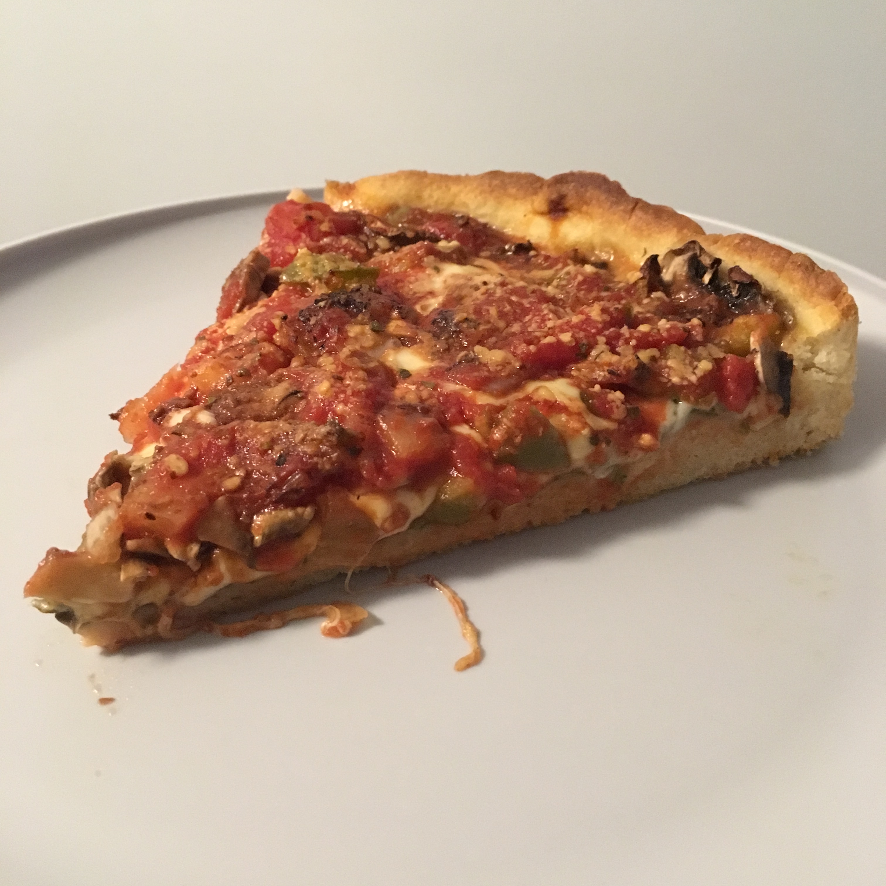 A slice of deep dish Chicago style pizza on a white plate.