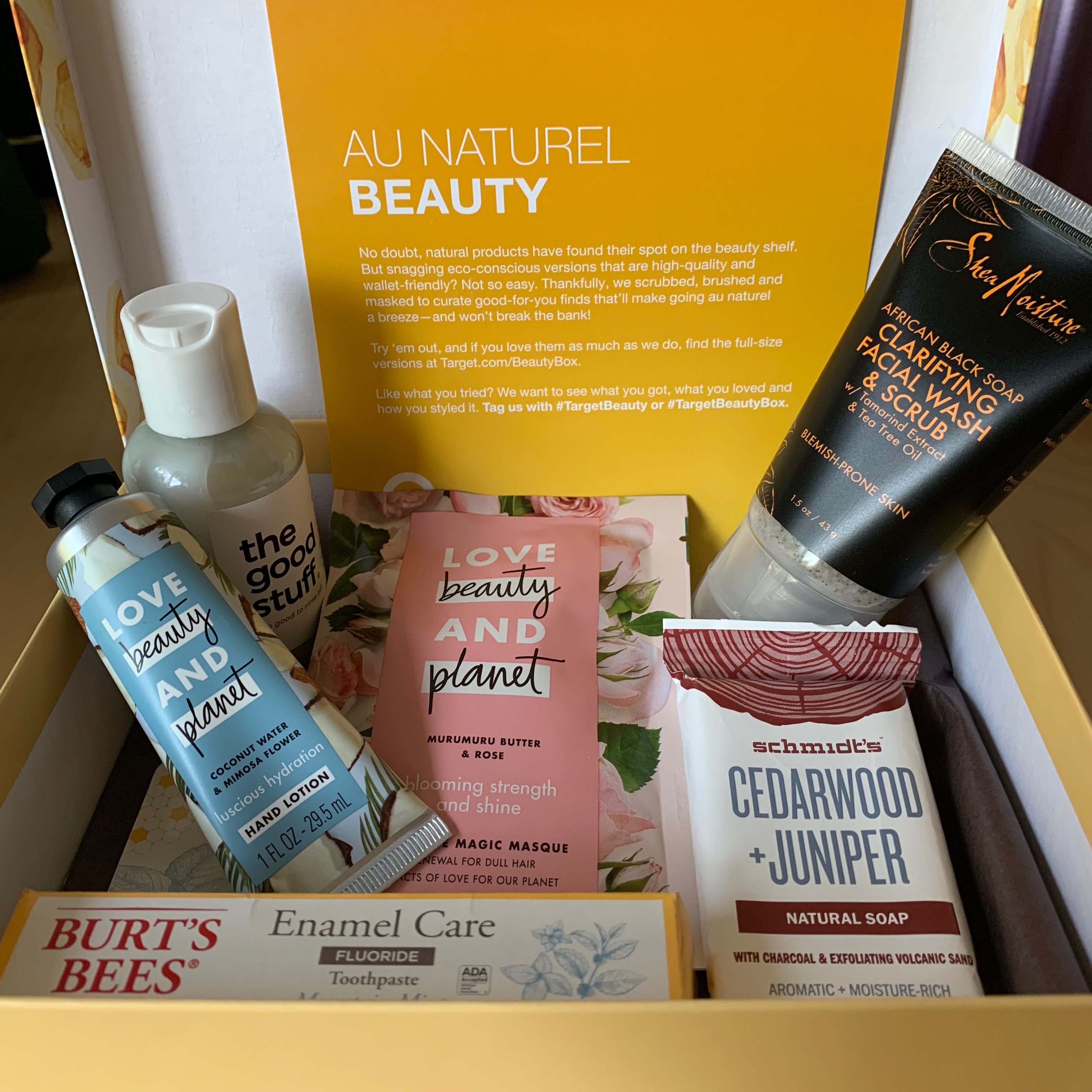 A box filled with 'natural' beauty products: facial wash/scrub, a small bar of soap, a hair mask packet, hand lotion, a mini toothpaste, and leave in conditioner.