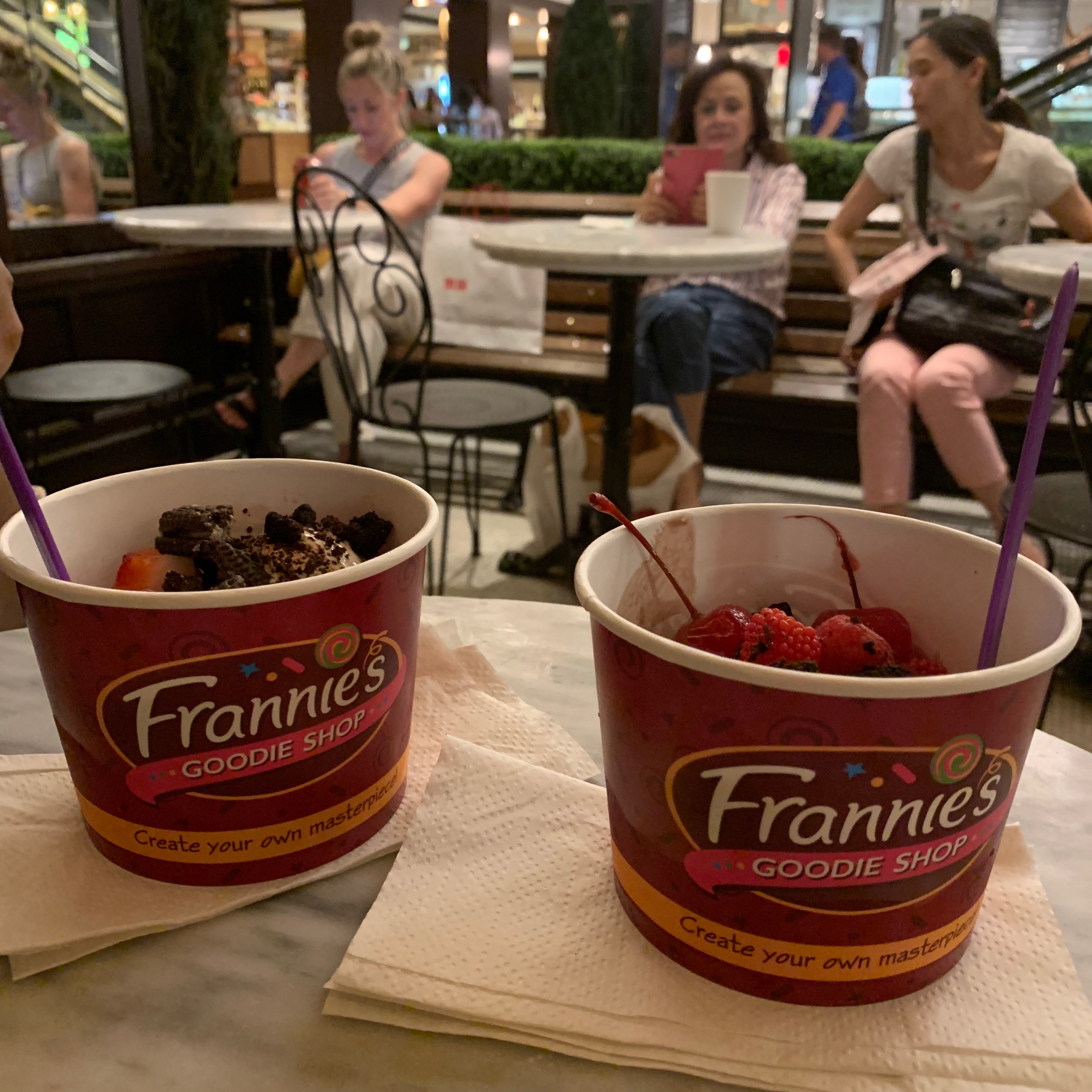 Two cups of frozen yogurt filled with chocolate and fruit on a table at the Plaza Food Hall.