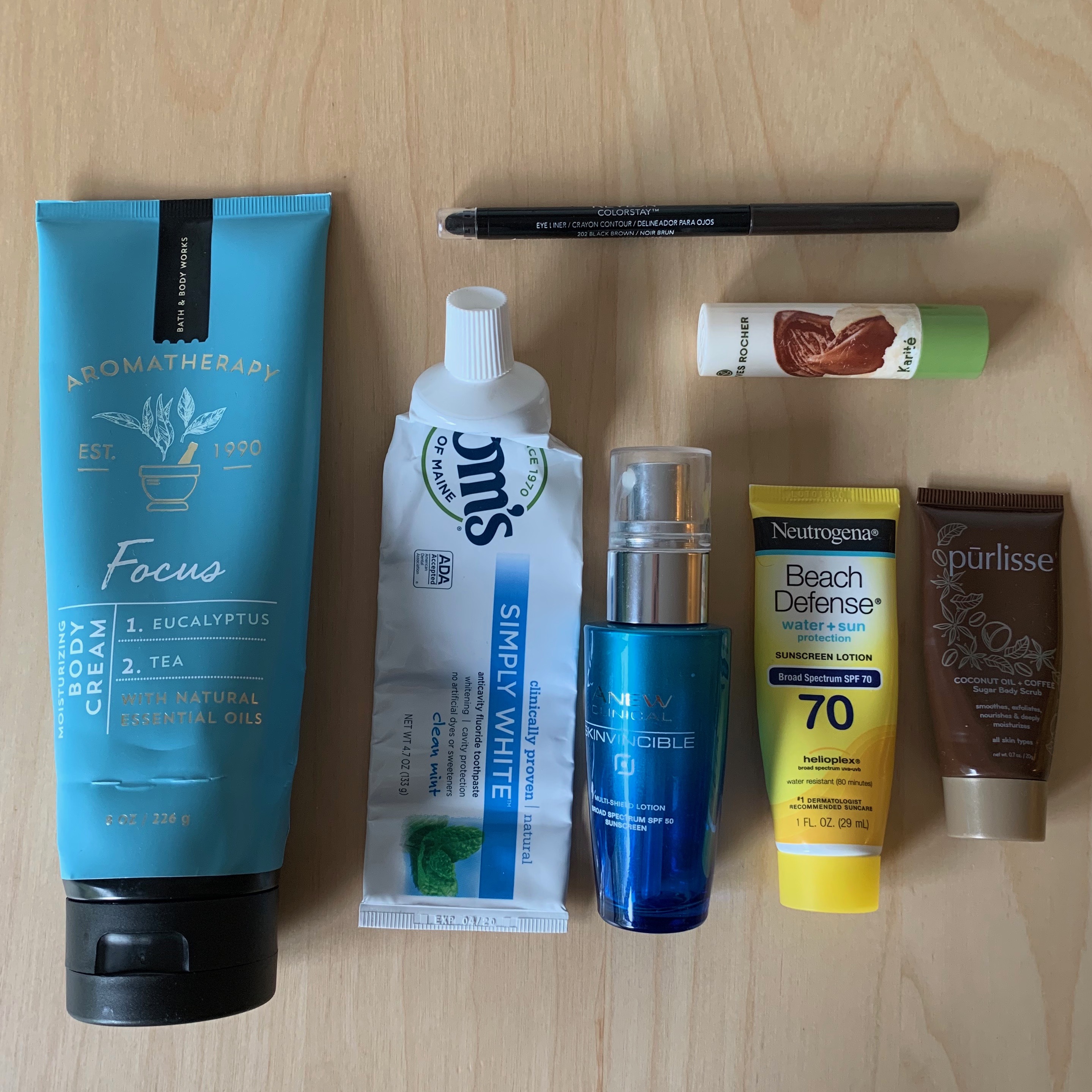 A photo of empty products that I used up in June: a full size lotion, two small sunblocks, a tube of toothpaste, an eyeliner, a lip balm, and a sample body scrub.